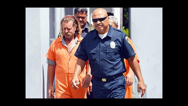 Dean J. Fletcher (left) is escorted by a police officer after his initial appearance in District Court yesterday. According to media reports, Fletcher is wanted by Tongan authorities for murder in the island Kingdom.  [photo: AF]