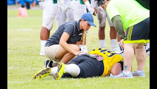 Certified Athletic Trainer (ATC) Florence Wasko (left) tending to one of the injured Nu’uuli Wildcats football players during week two of ASHSAA Football action this season. Every game so far has seen injuries — some season-ending, others from ‘old’ injuries, while others are concussions. [photo: TG]