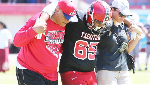 An injured Faga’itua player is escorted off the field by Vikings coach Jimmy Grey and ATC Florence Wasko during the Vikings vs. Warriors JV match last Saturday. [photo: TG]
