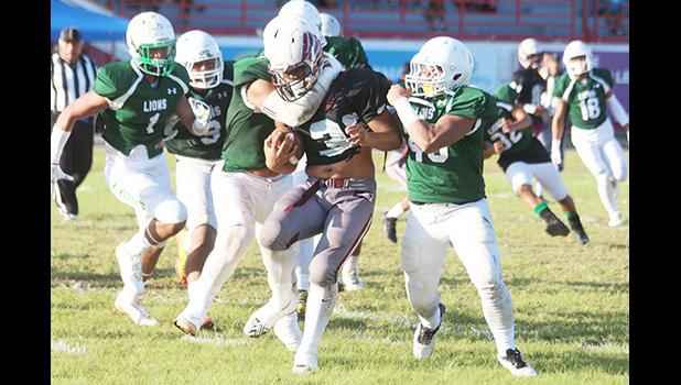 Ben Tuimaseve of Tafuna is stopped immediately by a host of Lions behind the line of scrimmage during the opening quarter of their varsity match last Friday evening, where Tafuna was handed their second loss of the season, 26-44. [photo: TG]