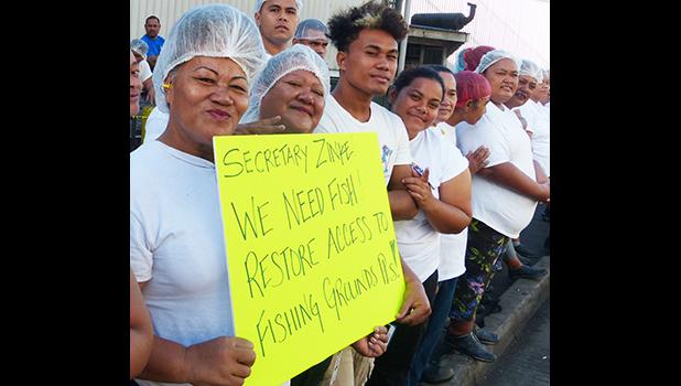 Cannery workers hold up sign reading "We need fish, restore access to fishing grounds, pls!"