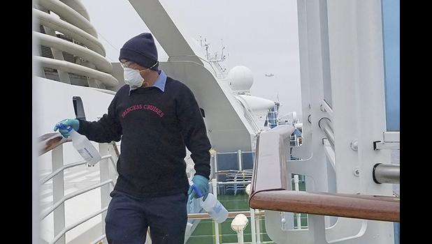 In this photo provided by Michele Smith, a A Thursday, March 5, 2020, off the California coast. Scrambling to keep the coronavirus at bay, officials ordered a cruise ship with about 3,500 people aboard to stay back from the California coast Thursday until passengers and crew can be tested, after a traveler from its previous voyage died of the disease and at least two others became infected. (Michele Smith via AP) A cruise ship worker cleans a railing on the Grand Princess