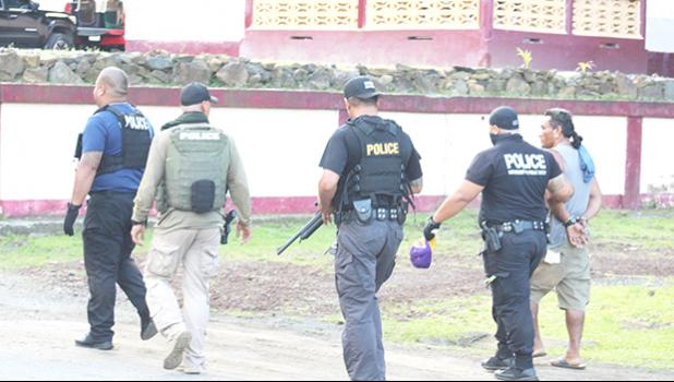 Police officers leading a suspect away on Monday after executing a search warrant on a compound in Aua. Police officers leading a suspect away