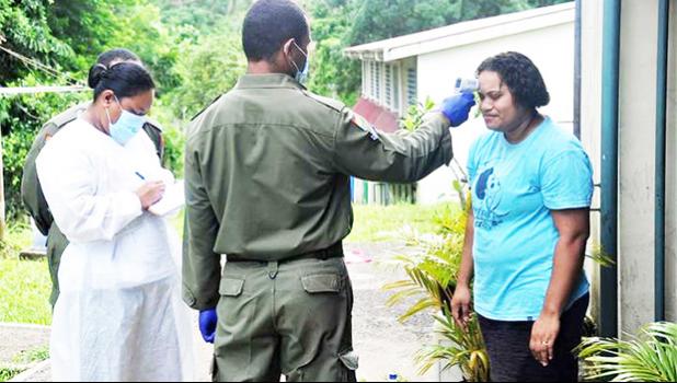 Soldier taking temperature of a woman in order to screen for COVID.