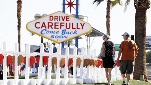 People walk by crosses placed near Las Vegas’ famous sign Thursday, Oct. 5, 2017, in Las Vegas. The crosses are in honor of those killed when Stephen Craig Paddock broke windows on the Mandalay Bay resort and casino and began firing with a cache of weapons at a country music festival Sunday. Dozens of people were killed and hundreds were injured. (AP Photo/Gregory Bull) 