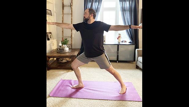 In this March 19, 2020, photo made available by Steve Latart, Latard does yoga exercises at his home in Rogers, Minn. LaTart's yoga and warrior sculpting instructors at Life Time Fitness in Minneapolis are still teaching classes. They've just moved them from the gym to cyberspace, where they are livestreaming instructions from their website. LaTart says knowing he can still participate in the classes is keeping him sane. (Steve Latart via AP) In this March 19, 2020, photo made available by Steve Latart, Latard does yoga exercises at his home in Rogers, Minn.