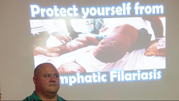A Health Department official standing in front of a screen — in the background — showing a photo of a person affected with Lymphatic Filariasis
