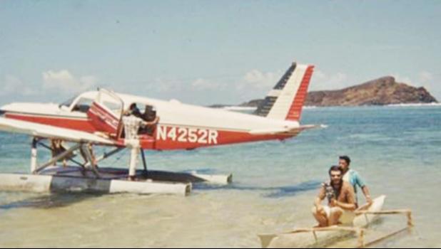 A Cherokee 6 on floats with a small paopao with 2 people in it beside the aircraft.
