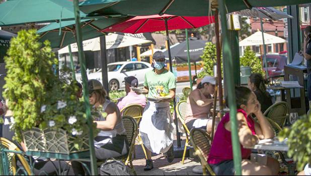 A waiter in a face mask delivers food to the tables outside of a restauran
