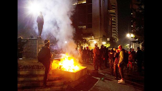 In this July 4, 2020, file photo, protesters gather near a fire in downtown Portland, Ore