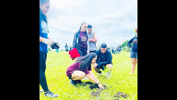 A student planing a tree while others look on.