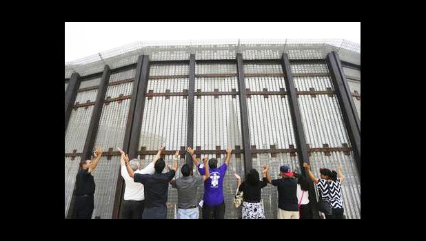 In this July 14, 2013, file photo, pastors and others raise their arms on the San Diego side of a border fence during a cross-border Sunday religious service with others on the Tijuana, Mexico side of the fence. The AP reported Sept. 8, 2017, that a story claiming Congress had approved President Donald Trump's request for $1.6 billion in border wall funding is false. (AP Photo/ Gregory Bull, File)