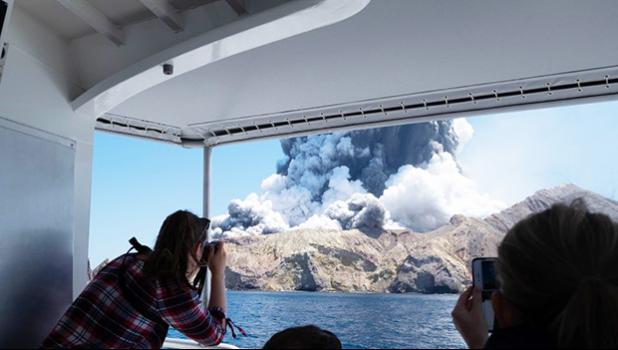 Tourists on a boat look at the eruption of the volcano