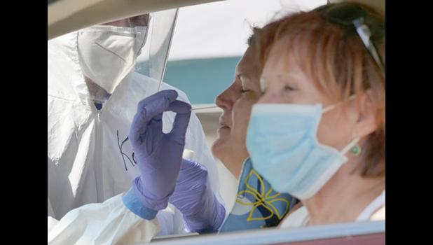 A woman sitting in a car administers a swab to her nose.
