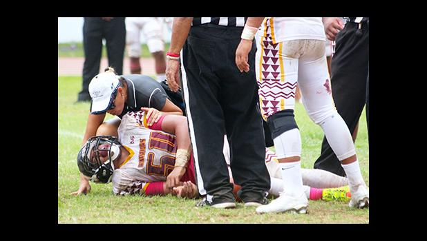 ATC Florence Wasko tending to the injured So’oso’o Letuli, Warriors middle linebacker, as he came down with a shoulder injury, in the second half of their varsity game against the Lions last Saturday – Letuli came back later to help the Warriors in their 20 - 6 win over Leone — keeping their No.1 seed heading into playoffs. [photo: TG]