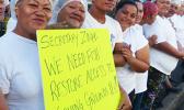 Cannery workers hold up sign reading "We need fish, restore access to fishing grounds, pls!"