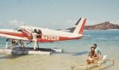 A Cherokee 6 on floats with a small paopao with 2 people in it beside the aircraft.