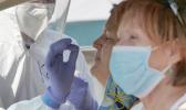 A woman sitting in a car administers a swab to her nose.